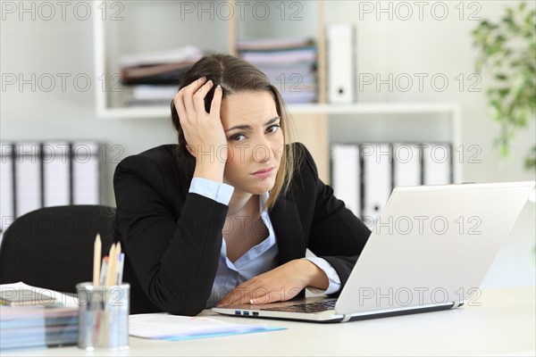 Worried office worker looking at camera sitting in a desk at workplace