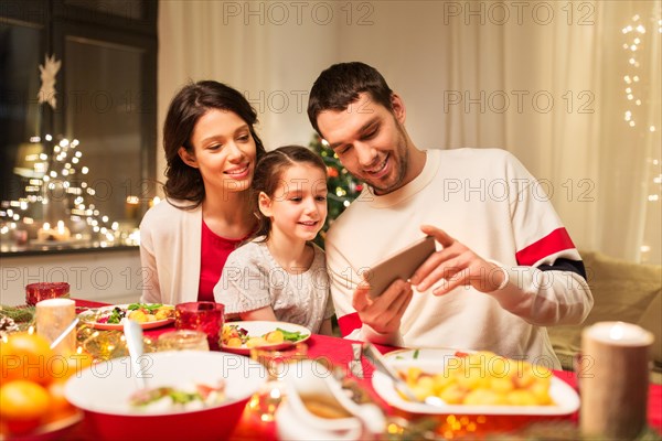 family with smartphone having christmas dinner