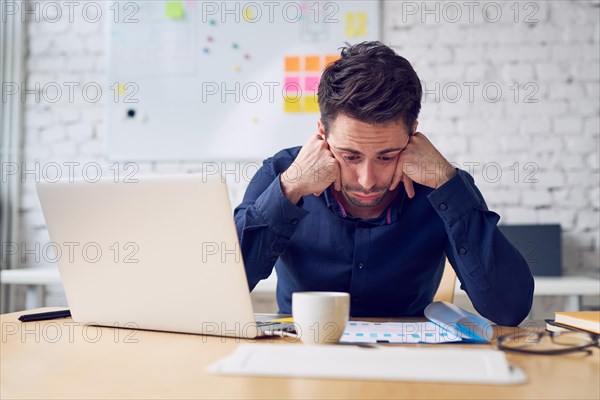 Depressed young man looking on financial documents working at office