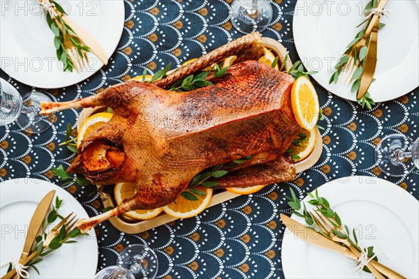 Festive table setting with whole roasted goose on a golden tray for celebrate event or Christmas family dinner. Top view, flat lay.