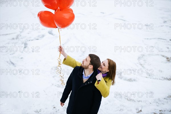 caucasian couple take a walk at winter street, celebrating saint valentines day outdoors. happy man and woman with red air balloons, on a romantic dat