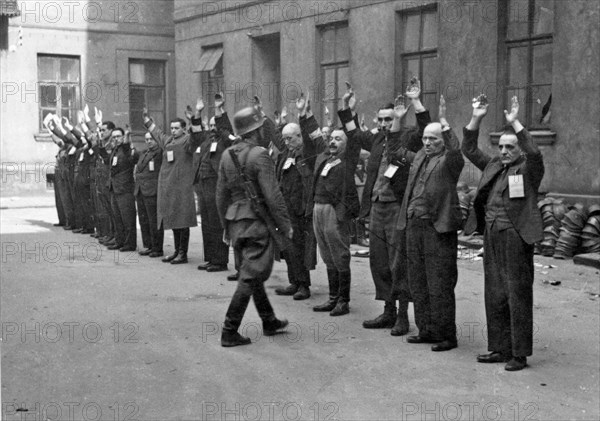 Warsaw Ghetto Uprising: Photograph of SS troops arresting the Jewish department heads of the Brauer helmet factory ca. April 24, 1943. The Brauer "shop", of Herman Brouer, made helmets for the German Army, was located at Nalewki 28-38 street and employed 2 thousand people.[3] Their workers were probably of the last Jews to be deported from the ghetto. With the outbreak of the uprising on April 19, 1943, Hermann Brauer promised those Jewish work managers who hadn't gone into hiding, that the factory would continue to operate, and asked that they come to work. These managers received special tra