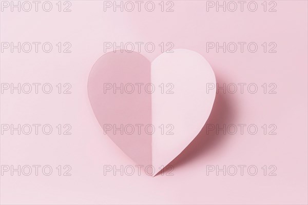 Love message or Saint Valentine Day conceptual flat lay. Top view on cut and curved paper pink heart with shadow on pink background. Minimalistic mockup for valentine card, invitation or greeting card
