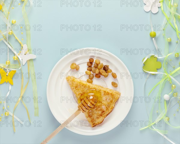 Homemade fried crepe with honey and raisins on a white plate with holiday decoration on a blue background with copy space. Russian national food. Chil