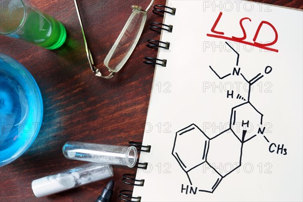 Notepad with chemical formula of LSD on the wooden table. Drugs concept.