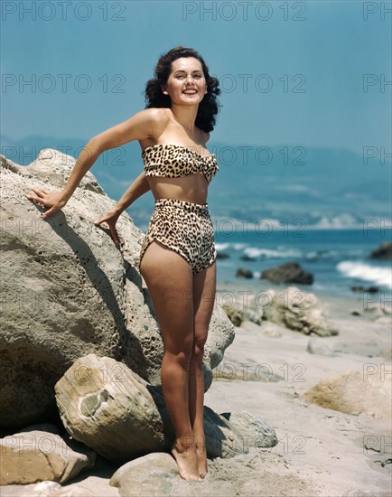 1940s BRUNETTE WOMAN LEOPARD SKIN TWO PIECE BATHING SUIT STANDING ON ROCKY BEACH