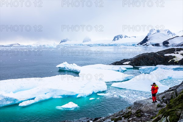 Tourist taking photos of amazing frozen landscape in Antarctica with icebergs, snow, mountains and glaciers, beautiful nature in Antarctic Peninsula w