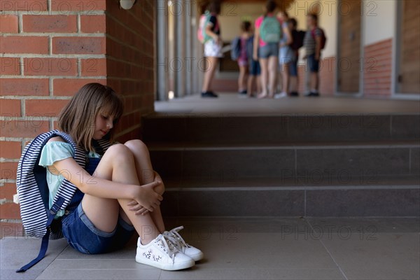 Schoolgirl  sitting on the ground alone in the schoolyard at elementary school