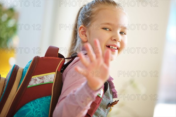 Smiling child with satchel goes to school and waves goodbye