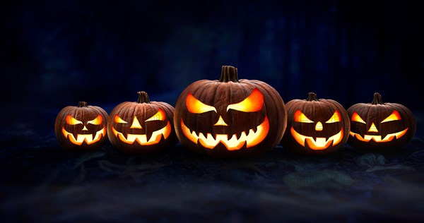 Five spooky halloween pumpkin, Jack O Lantern, with an evil face and eyes on the forest floor at night with a dark background.