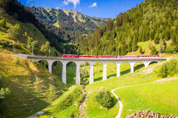 Bright sun over Glacier Express train traveling on Tujetsch viaduct in summer, Sedrun, Graubunden canton, Switzerland