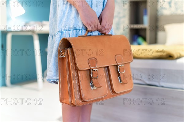 Girl holding a classic leather school bag in her bedroom in a close up view