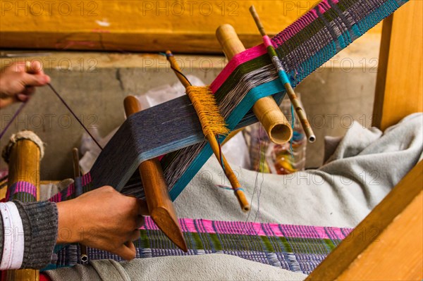 A Bhutanese woman weaving fabric on a wooden loom by hand in Bhutan.
