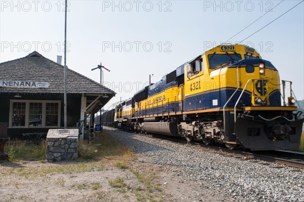 A train engineer waves out the window as his Alaska Railroad train engine passes the railroad station in Nenana, Alaska, USA