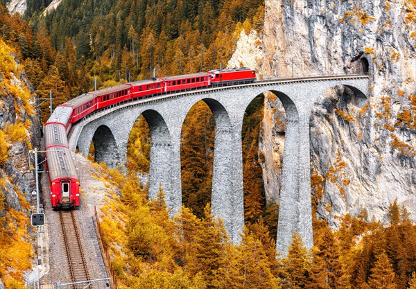 Bernina express glacier train on Landwasser Viaduct in autumn, Switzerland. Scenic view of railroad bridge in orange mountain forest in Swiss Alps. Th
