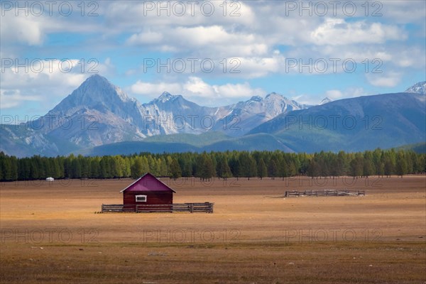 House in the countryside with the mountains in the background. Farm cabin in the rural country surrounded by forest and hills with the snowy tops.