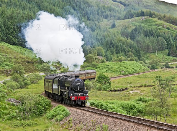 Jacobite steam train moves up hill beyond Glenfinnan Station towards Mallaig on a sunny summer day
