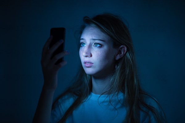 A young woman using an iPhone smart phone looking worried anxious concerned cyber bullying bullied on-line