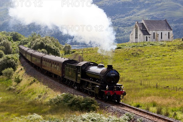 Jacobite Steam Train passing Our Lady of the Braes Church at  Polnish Highlands Scotland UK