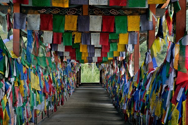 BHUTAN - Prayer flags cover the inside of the Kundeyling Baazam (a cantilever pedestrian bridge) crossing the Wang Chhu (river).