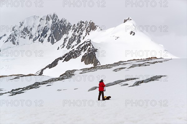 One person standing on the ice in front of a snow-covered mountain.