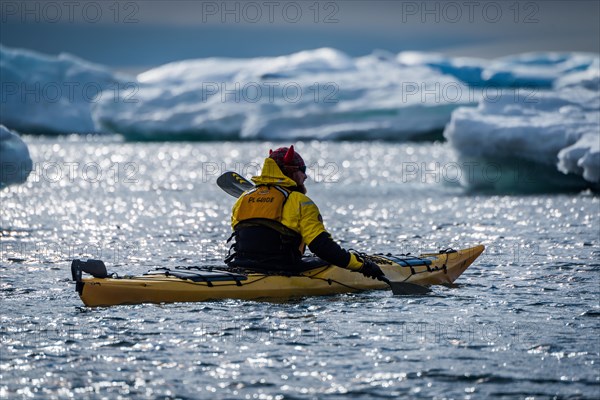 Backlit kayaker paddling past icebergs in sunshine