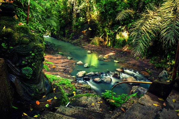 Secret waterfall hidden in tropical jungle with traditional old stone statue on background scenery nature