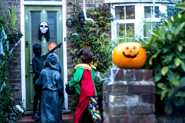 Three boy in halloween costumes, standing at door, trick or treating, rear view