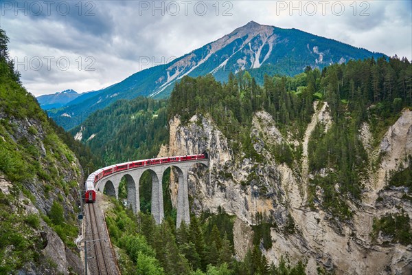 Red train passes above the Landwasser Viaduct bridge, in canton of Graubünden, Switzerland. Bernina Express / Glacier Express uses this railroad.