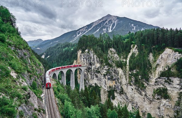 Red train passes above the Landwasser Viaduct bridge, in canton of Graubünden, Switzerland. Bernina Express / Glacier Express uses this railroad.