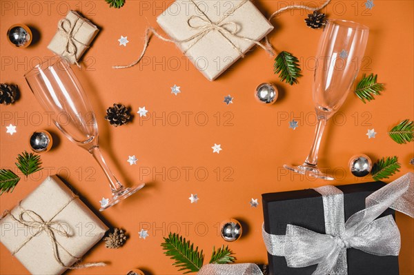 Christmas holiday composition. Handmade gift boxes decorated with craft paper of fir tree branches, two glasses champagne, pine and confetti on orange