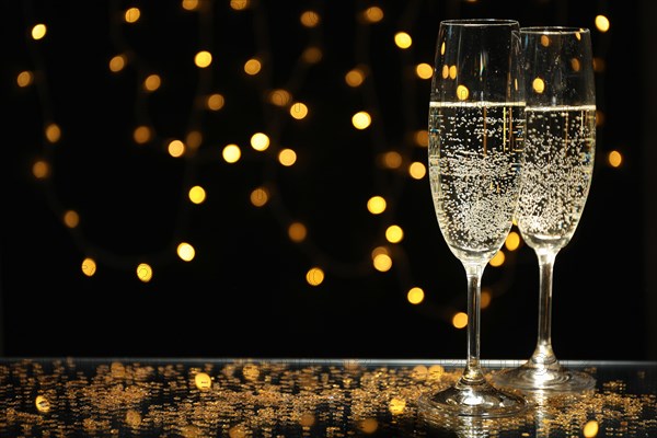 Champagne glasses against blurred lights background, space for text