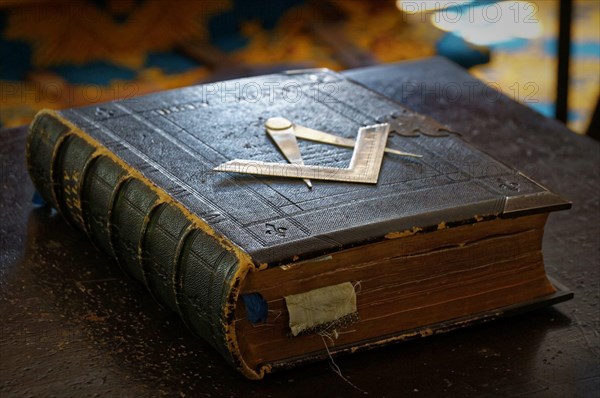 Ancient Masonic Holy Bible book with darkened pages and old bookmarks in dark brown leather cover with Square and Compass metallic symbol on the cover