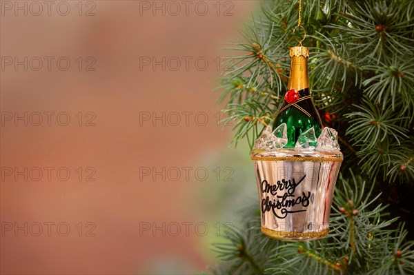 Christmas ornament champagne bottle in a bucket of ice hanging from a fir tree. Copy space.