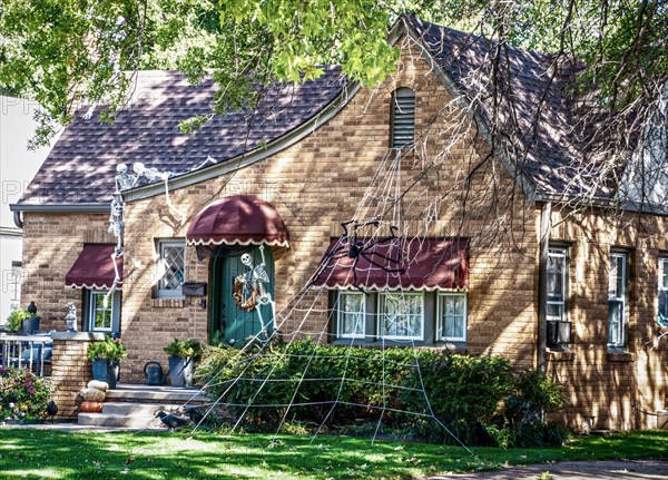 Spooky vintage cottage with awnings is decorated for Halloween with skeletons crawling on roof and huge spider web