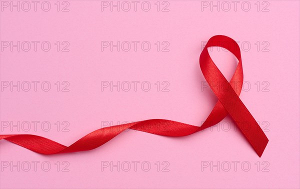 A silk red ribbon in the form of a bow on a pink background, a symbol of the fight against AIDS and a sign of solidarity and sup