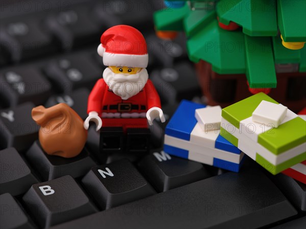 Tambov, Russian Federation - October 31, 2023 A Lego Santa Claus minifigure sitting on a computer keyboard next to Christmas tree and some presents. C