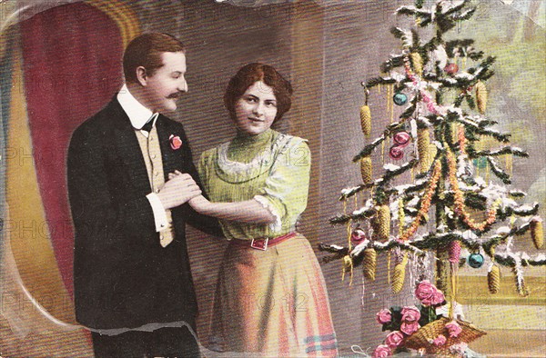 Vintage Christmas greeting card from 1910 with loving couple near small tree