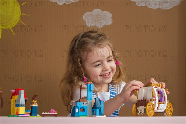 Cute funny preschooler little girl playing with construction toy blocks in kindergarten room. background painted by the sun and clouds