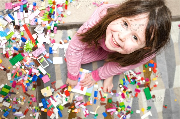 Young smiling girl looking at camera playing with lego