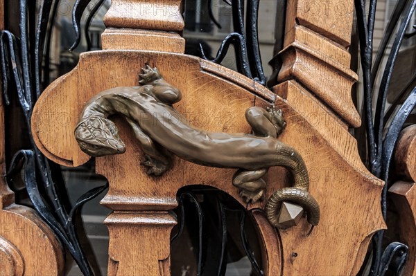 Ornate art nouveau wooden door detail with organic motif and a bronze figurine of a lizard for a door handle in Paris, France