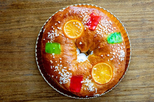 Christmas round fruit cake decorated with fir tree branch, glazed fruits and nuts on a wooden background.