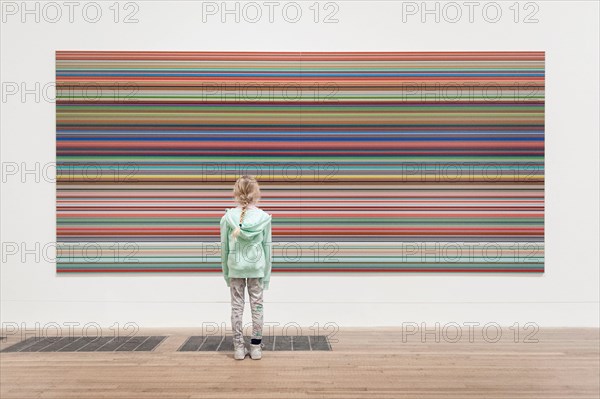 A girl stands in front of a large Bridget Riley painting in the Tate Modern Art Gallery.