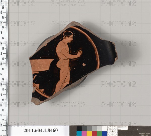 Terracotta fragment of a stemless kylix (drinking cup) 460–450 B.C. Greek, Attic Interior, filleted youth to right, holding a fillet in his right hand; behind him, a laver, on two steps; Exterior, start of handle root; torus foot; the resting surface and the inner wall of the foot are glazed; the underside of the floor has a wide band of black glaze, and a thin circle of reserve, followed by a thin band of black glaze; the center is in reserve, with a small black glaze circle in the middle with a dot in the center. Terracotta fragment of a stemless kylix (drinking cup). Greek, Attic. 460–450 B