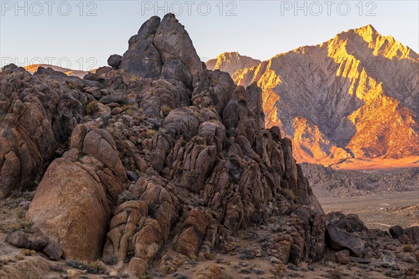 Ancient rock formations of Alabama Hills in foreground with desert expanse and Sierra Nevada mountains in background with alpenglow