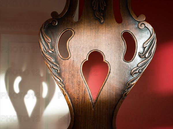 Antique wood chair back with cut out decoration in the shape of a cartoon face. Corresponding face shadow in the background.