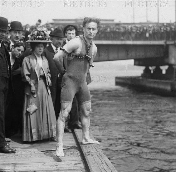 Houdini jumps from Harvard Bridge, 1908, Houdini standing by the side of the Charles River wearing chains and handcuffs.
Harry Houdini (1874 – 1926) Austro-Hungarian-born American Escape Artist, illusionist and stunt performer