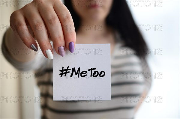 Young sad girl shows a white sticker. Caucasian brunette holding a sheet of paper with message. Metoo hashtag .