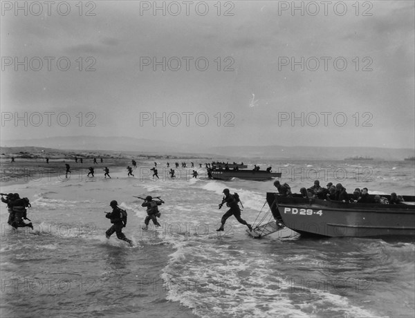 Invaders Hit the Shore in Invasion Maneuvers - American troops, carrying rifles and light fighting equipment, spring through the surf from Coast Guard-manned landing craft in final amphibious maneuvers somewhere on the North African coast. Invaders and Coast Guard invasion craft, such as these, hit the beaches of French Normandy before dawn D-Day