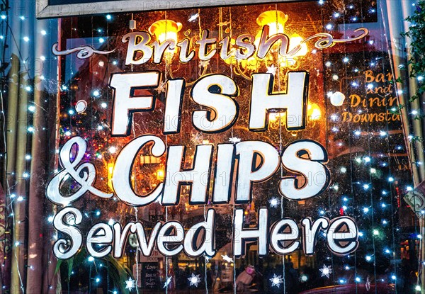 Fish and chips sign warm welcoming with frosty snow effect in winter, sign on traditional London pub window with welcoming warm festive twinkling lights at night Traditional British food in winter served in a typical London Public House